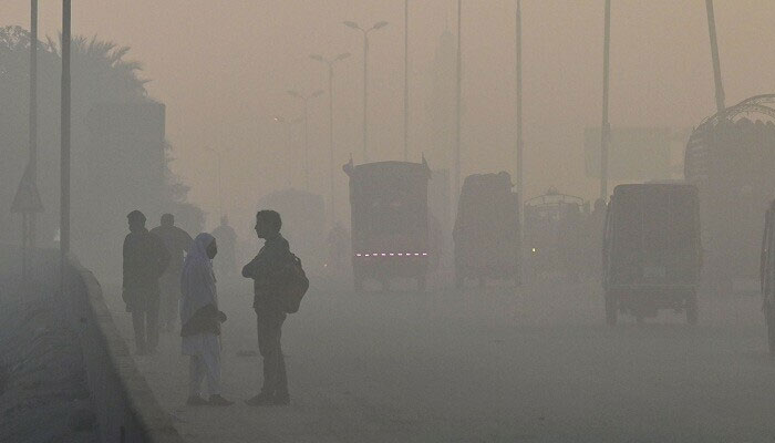 Students (L) wait for transport alongside a road amid heavy smog conditions in Lahore. — AFP/File