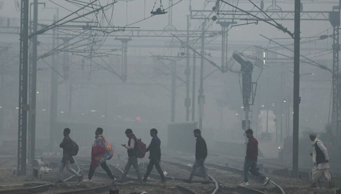 People cross railway tracks on a smoggy morning in New Delhi, India, November 3, 2023. — AFP