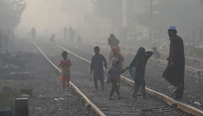 People walk on a railway track amid smoggy conditions in Lahore on November 16, 2021. — AFP