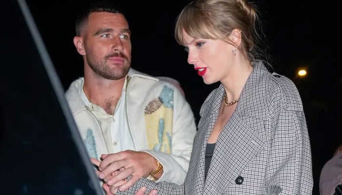 Travis Kelce looks at Taylor Swift as they walk to sit in a car. — X/@grosbygroup