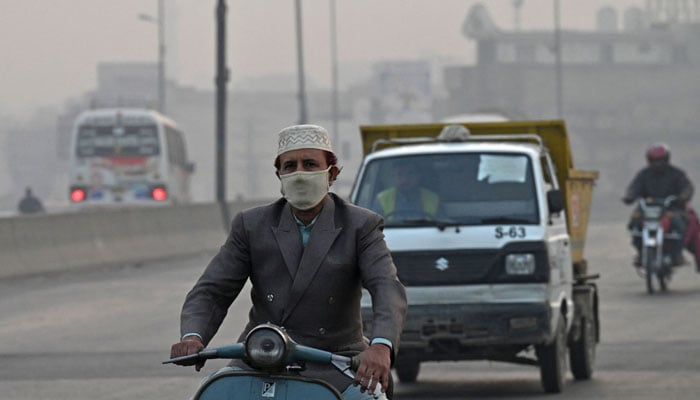 A man wearing a face mask rides a bike, amid smoggy conditions in Lahore on November 21, 2023. — AFP