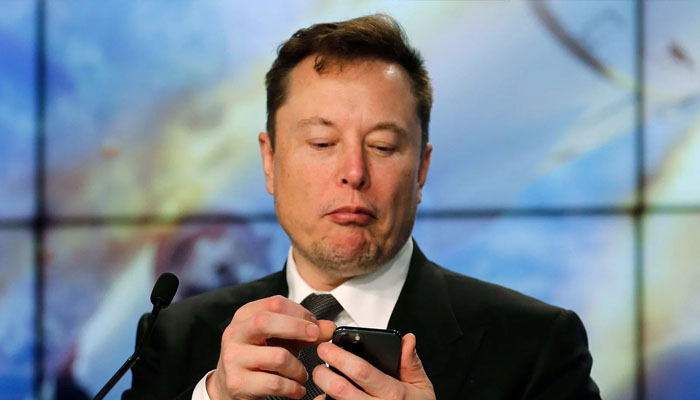 Elon Musk gestures while looking at phone. — X/@alamy