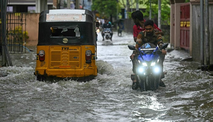 Commuters wade across a flooded street after heavy rains ahead of Cyclone Michaung´s landfall in Chennai on December 3, 2023. — AFP