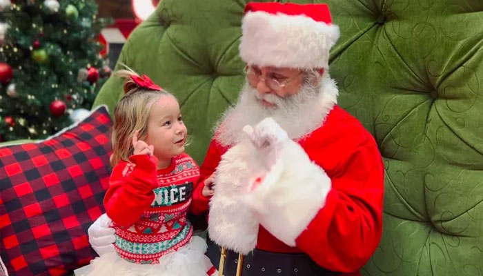 Charles Graves interacts with a child using sign language while dressed as Santa Claus. — People