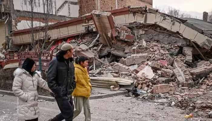 People walk past a collapsed building after an earthquake in Dahejia, Jishishan County in northwest Chinas Gansu province on Tuesday. — AFP