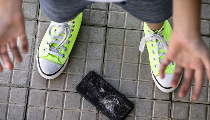 A broken phone on the pavement with a person standing near it. — X/@rhj