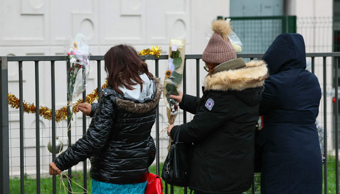 People lay flowers just in front of the ground floor flat where the bodies of a woman and her four children were discovered, in Meaux, eastern Paris, on December 26, 2023. — AFP