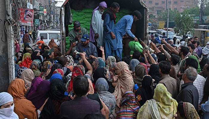 People show their NICs to receive free bags of flour from a delivery truck at a distribution point in Lahore on March 20, 2023. — AFP