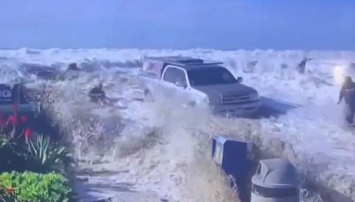 The screenshot shows people and a vehicle parked over the seashore being washed away by huge waves. — x/accuweather