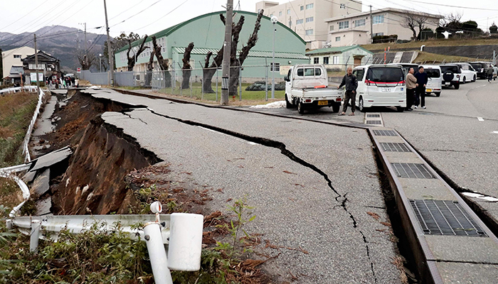 People stand next to large cracks in the pavement after evacuating into a street in the city of Wajima, Ishikawa prefecture on January 1, 2024. — AFP
