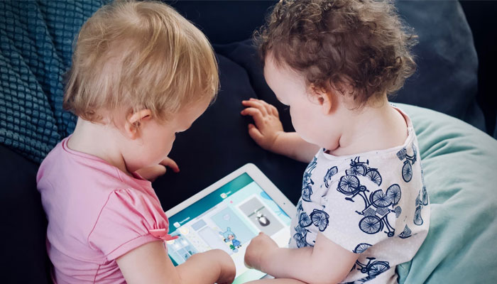 Two toddlers playing on a tablet. — Unsplash