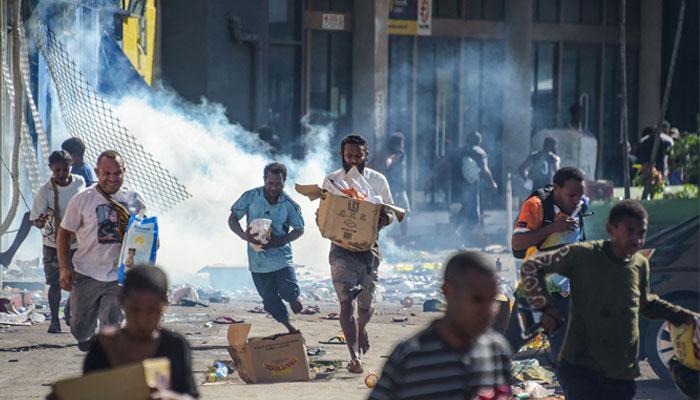 People run with merchandise as crowds leave shops with looted goods amid a state of unrest in Port Moresby on January 10, 2024 — AFP