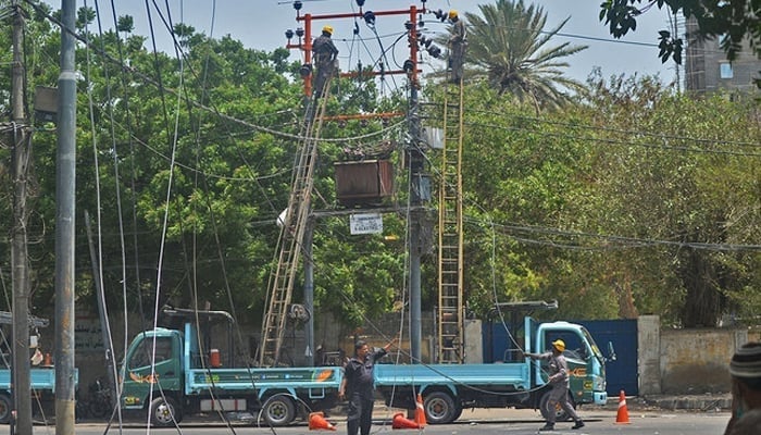 Men work on electric pylons along the roadside in Karachi on May 30, 2021. — AFP/File