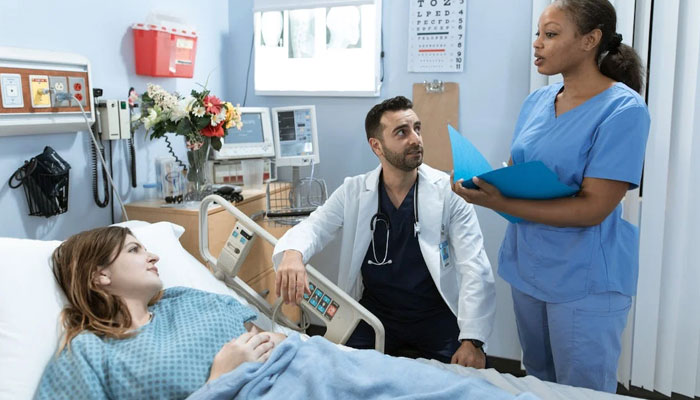 This image of a doctor, pictured as male, talking to a nurse, pictured as female about the patient, is an example of a gender stereotype. — Pexels