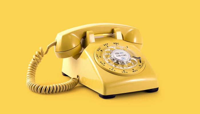 The image shows a yellow-colored landline phone. — Unsplash