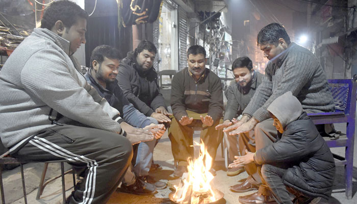 Shopkeepers sit around a bonfire at a local market during a winter night in Lahore on December 30, 2023. — Online