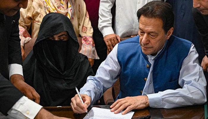 Former prime minister Imran Khan (right) along with his wife Bushra Bibi signs surety bonds for bail in various cases in Lahore High Court on July 17, 2023. — AFP