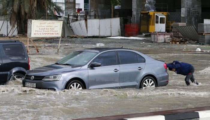A man pushes his car through flooded roads in the United Arab Emirates. --AFP/File