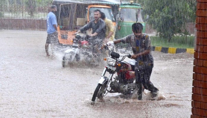 A youngster is pushing his motorcycle through rainwater during heavy rain in Multan on August 26, 2023. —APP