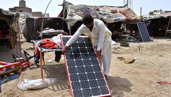 A man props a solar panel against a cot. — APP/File