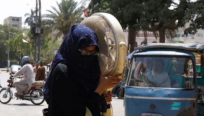 A woman carries a pedestal fan for repair during hot and humid weather. — Reuters/File