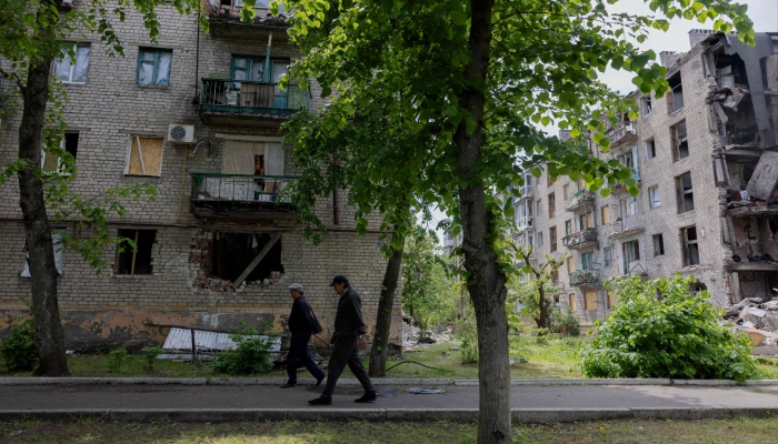 Men walk past a damaged residential building in the town of Lyman, near the frontline in the Donetsk region, on May 7, 2025 amid the Russian invasion of Ukraine. — AFP