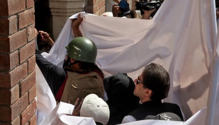 Pakistans former Prime Minister Imran Khan and his wife Bushra Bibi are covered with a white sheet as they arrive to appear at the High Court in Lahore, Pakistan, May 15, 2023 — REUTERS