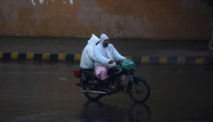Commuters ride on a motorbike along a road during rainfall in Karachi. — AFP/ File