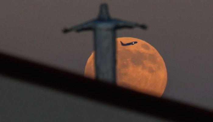 Plane appears between the Harvest Supermoon and a statue of Jesus Christ atop Iglesia Luterana Santa Maria de Guadalupe, Dallas