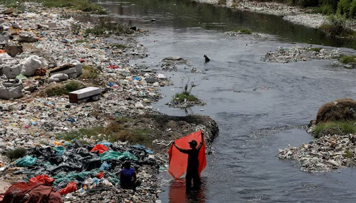 A man washes waste plastic sheets, collected for recycling, in the polluted waters on World Environment Day in Karachi, Pakistan June 5, 2023. — Reuters